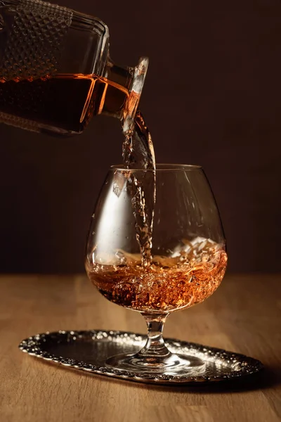 Brandy is poured from a decanter into a snifter glass. Cognac on an oak table.