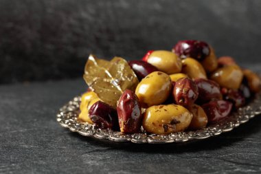 Spicy olives in a silver dish on a black stone table.
