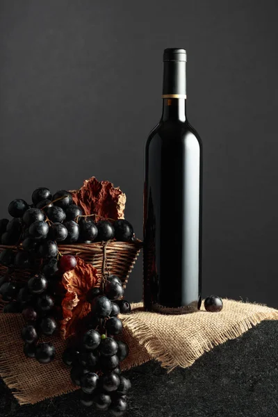 Juicy blue grapes and a bottle of red wine on a black background.