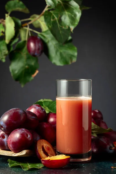 Glass of plum juice on a table with fresh purple plums.