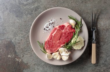 Biberiye, sarımsak, tuz ve biberli çiğ biftek. Eski taş arka plan. Üst görünüm.