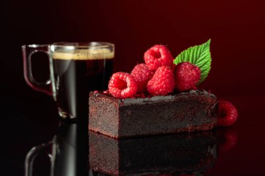 Chocolate cake with fresh raspberries and black coffee on a dark red background.