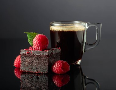 Chocolate cake with fresh raspberries and black coffee on a black reflective background.