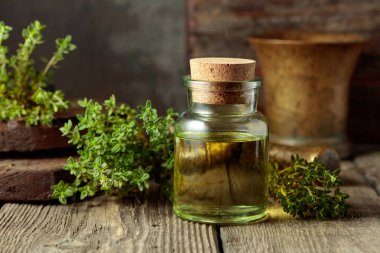 Bottle of thyme essential oil with fresh thyme twigs on an old wooden table.