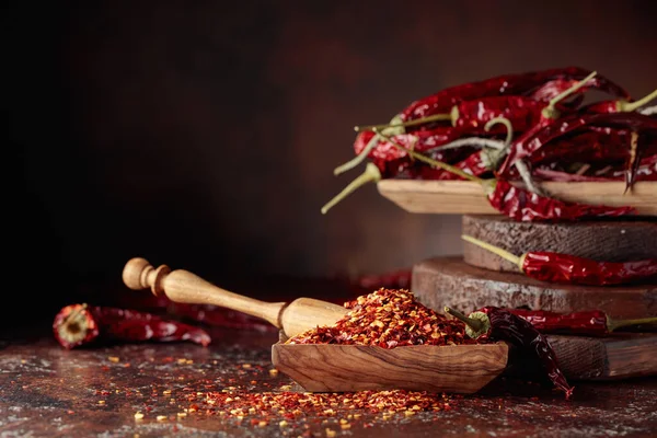 Chilli flakes and dried chili peppers on a brown table.