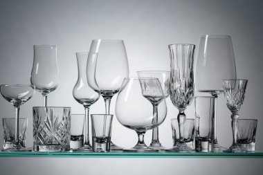 Silhouettes of different empty glasses on a glass shelf.