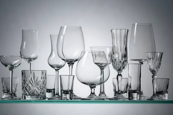 Silhouettes of different empty glasses on a glass shelf.