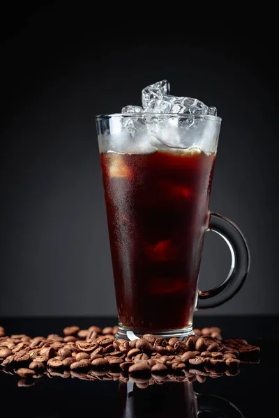 Ice coffee and coffee beans on a black reflective background. Copy space.