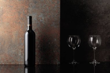 Paslı kahverengi arka planda boş şarap kadehleri olan bir şişe kırmızı şarap. Metnin için alanı olan ön görünüm.