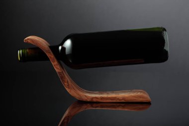 Bottle of red wine in a wooden bottle holder on a black reflective background. Copy space.