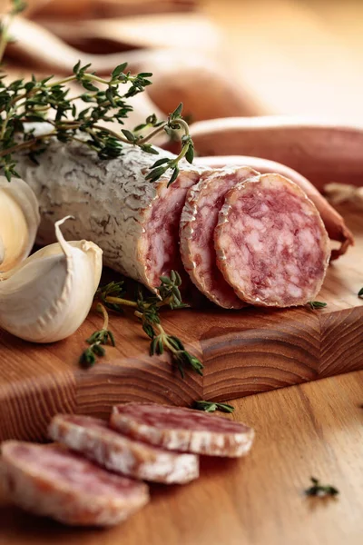 Traditional dry-cured sausage with thyme, garlic, and onion. Dry-cured sausage on a wooden table. Selective focus.