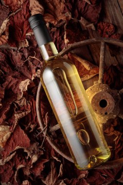 Bottle of white wine on the rusty wheel and dried-up vine leaves. Old expensive wine concept. Top view.
