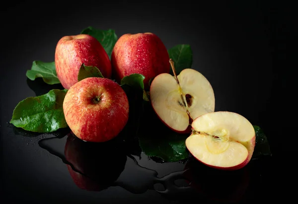 Juicy apples with leaves. Fresh apples with drops of water on a black reflective background.