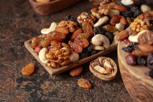 Mix of nuts and raisins on a brown rustic background. Presented raisins, walnuts, hazelnuts, cashews, pecans, and almonds. Selective focus.