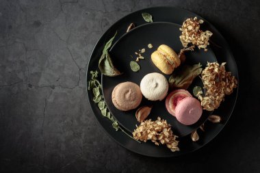 Siyah bir tabakta kurumuş çiçeklerle lezzetli, renkli badem kurabiyeleri. Üst Manzara. Boşluğu kopyala.