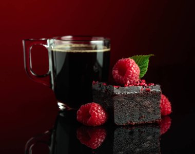 Chocolate cake with fresh raspberries and black coffee on a dark red background.