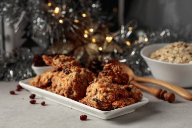 Ev yapımı yulaf ezmeli kurabiye ve Noel süslemeleri olan bir masada kuru üzüm..