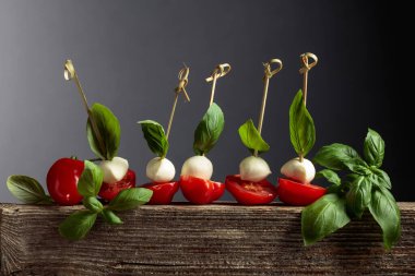 Eski bir tahta üzerinde fesleğen ve domatesli Mozzarella. Geleneksel İtalyan atıştırması.