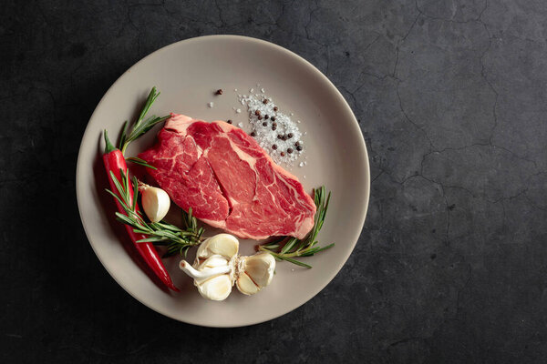 Raw beef meat steak for grilling with rosemary, garlic, salt, and pepper. Top view.
