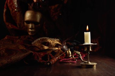 Pirinç bir şamdanda yanan mum ve eski ahşap bir masada karnaval maskeleri..