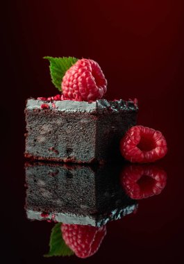 Koyu kırmızı arka planda taze ahududu ile süslenmiş çikolatalı pasta..