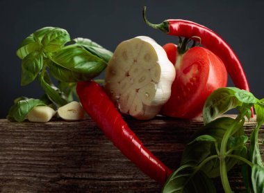 Baharatlı domates sosu yapmak için gerekli malzemeler. Eski ahşap bir masada taze domates, kırmızı biber, sarımsak ve fesleğen..