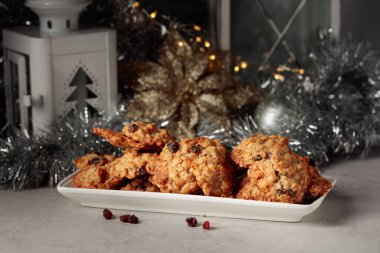 Ev yapımı yulaf ezmeli kurabiye ve Noel süslemeleri olan bir masada kuru üzüm..