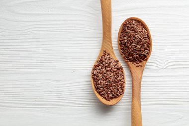 Beyaz ahşap arka planda keten tohumu olan tahta kaşıklar. Üst görünüm.