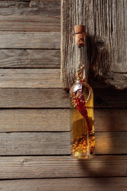 Ahşap arka planda küçük bir şişede otlar ve baharatlarla ev yapımı zeytinyağı. Boşluğu kopyala.