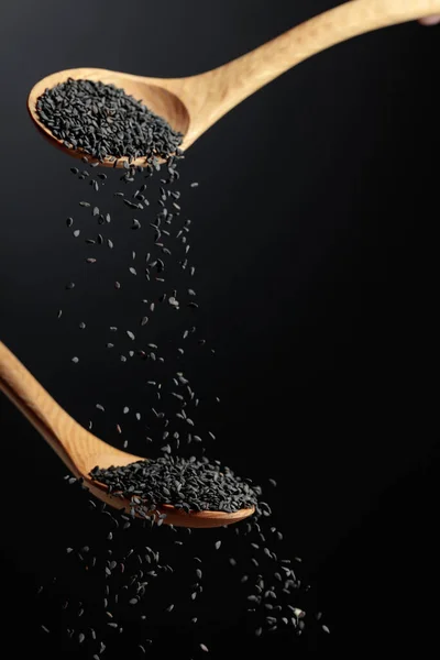Grains of black sesame are poured with wooden spoons. Black sesame on a dark background. Copy space.
