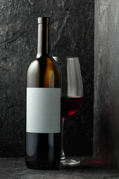 Red wine on a black stone background. On a bottle empty label for your text.