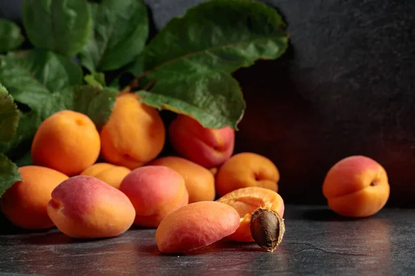 Apricots with leaves on a black stone table.