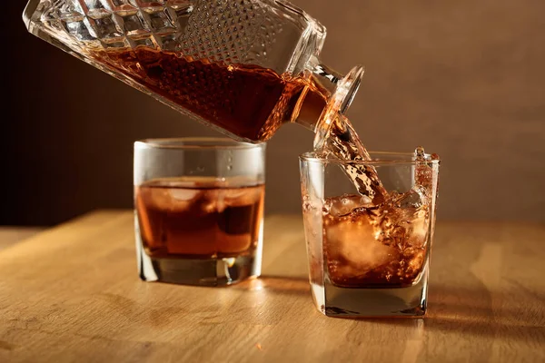 Whiskey is poured into a dammed glass with natural ice. Glass of whiskey on an oak table.