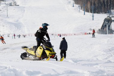 Koruyucu kıyafetli bir adam kışın beyaz karda kar motosikletine biner. Seçici odaklanma. 14.11.2020, Sheregesh, Rusya