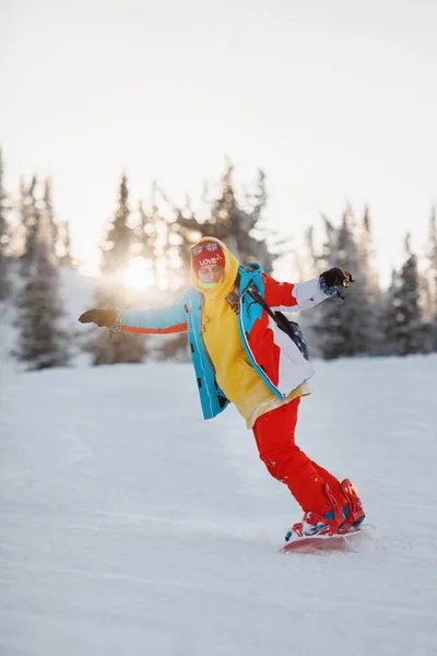 女性は天然のリゾートで雪の山の斜面でスノーボードをしています スキー用具 赤いズボンとニット帽 暖かい黄色のジャケット 選択的焦点 — ストック写真