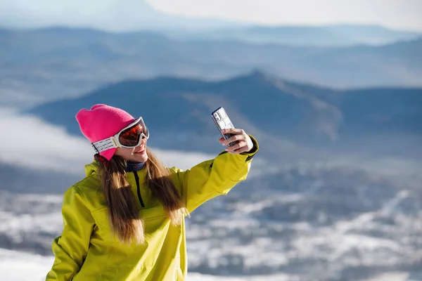 Kobieta Stroju Narciarskim Robi Sobie Selfie Tle Niebieskich Gór Żółta — Zdjęcie stockowe