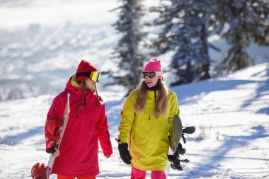 İki snowboardcu kar kaplı bir dağda yürür ve konuşurlar. Kayak kıyafetleri giyiyorlar: gözlükler, kırmızı ve sarı ceketler, örgü şapkalar. Sağlıklı bir yaşam tarzı. Spor konsepti. Seçici odak.