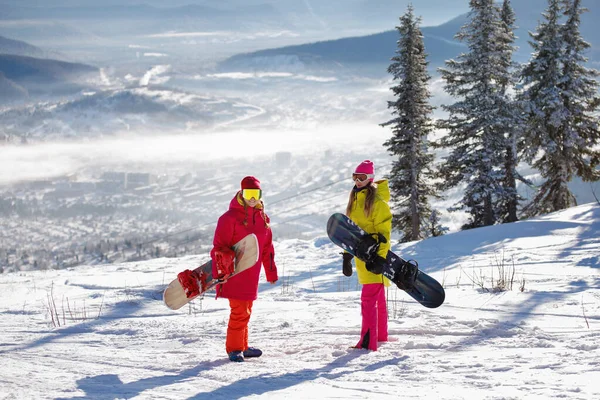 2人のスノーボーダーが立って青い山々の背景について話しています 彼らはスキー服を着ています 赤と黄色のジャケット ニット帽 健康的なライフスタイル スポーツの概念 選択的焦点 — ストック写真
