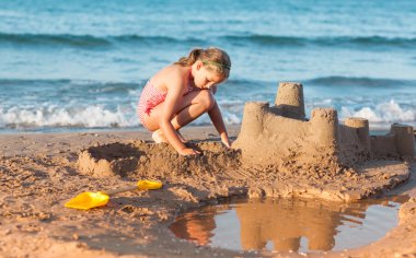 Child builds sandcastle on the beach clipart