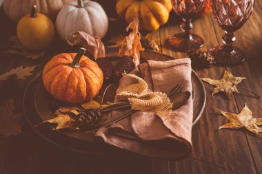 Autumn place setting with pumpkins, cutlery and golden leaves on a wooden table