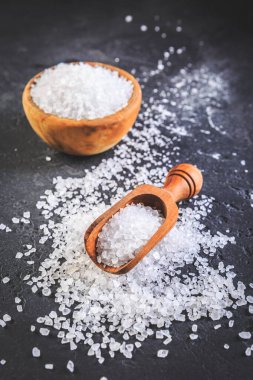 Tahta kasede saf deniz tuzu ve siyah arka planda tahta kaşık.