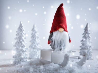 Şirin Noel cücesi kızağın üzerinde oturuyor, kışın beyaz ağaçlı. 