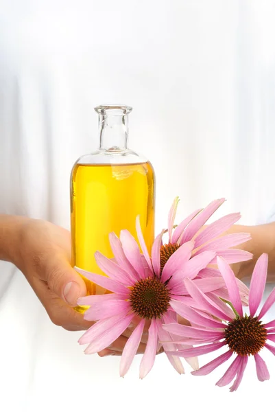 Manos de mujer joven sosteniendo aceite esencial y flores frescas — Foto de Stock