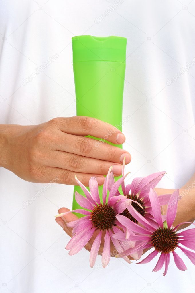 Hands of young woman holding cosmetics bottle and fresh coneflowers
