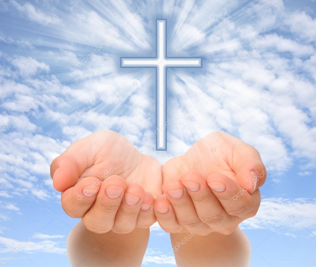 Hands holding Christian cross with light beams over sky