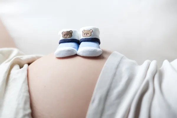 Gravid kvinna med två små Babyskor på magen — Stockfoto