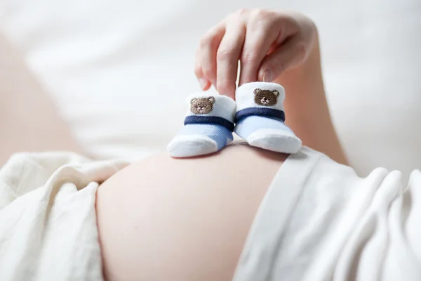 Pregnant woman with two little baby shoes on her belly — Stock Photo, Image