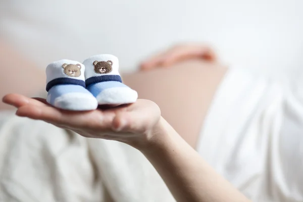 Pregnant woman with two little baby shoes on her hand — Stock Photo, Image