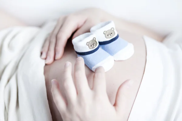 Mujer embarazada con dos pequeños zapatos de bebé en su vientre — Foto de Stock