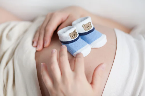 Schwangere mit zwei kleinen Babyschuhen auf dem Bauch lizenzfreie Stockfotos